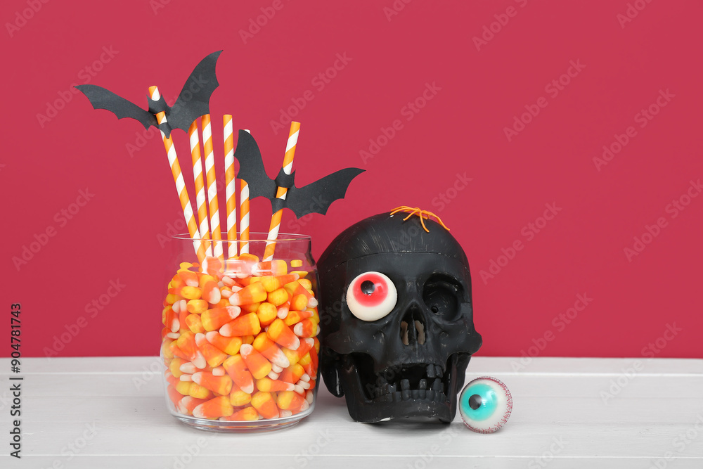 Wall mural black skull and glass jar with tasty candy corns for halloween celebration on light wooden table