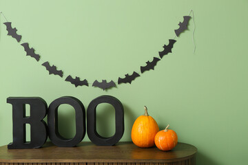 Halloween pumpkins with word BOO on commode near green wall in room