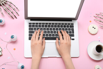 Female hands with laptop, cup of coffee and Halloween decorations on pink background