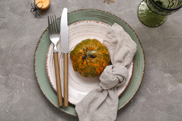 Festive table setting with Halloween pumpkin and spiders on grey grunge background
