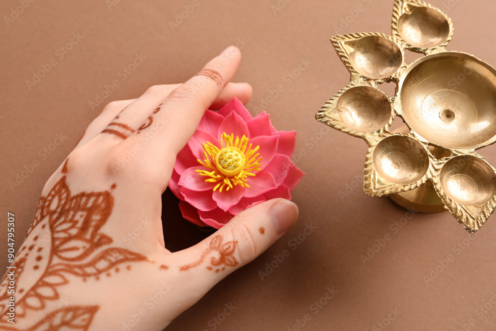 Wall mural Female hand with diya lamp and lotus flower for celebration of Divaly on brown background