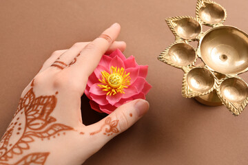 Female hand with diya lamp and lotus flower for celebration of Divaly on brown background