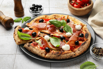 Tasty pizza with cured ham, olives, mozzarella cheese, tomatoes and basil on light tiled table, closeup