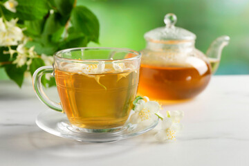 Aromatic jasmine tea in cup, flowers, teapot and green leaves on white marble table