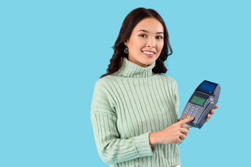 Fototapeta premium Young Asian woman with payment terminal on blue background