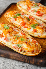 Cheesy Shrimp Garlic Bread with herbs and tomato closeup on the wooden board on the table. Vertical