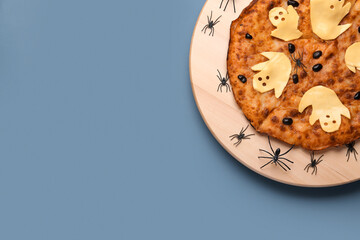 Wooden board with tasty pizza and spiders for Halloween party on blue background