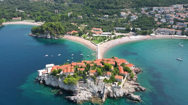 A drone flies over the famous island of Sveti Stefan in Montenegro on a sunny summer day