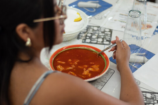 Female customer, eating a plate of menudo at a Mexican market in the market of authentic Mexican restaurants with traditional cuisines and recipes
