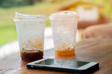 Close up ice cube in the glasses of coffee with phone on the wooden table after drink.