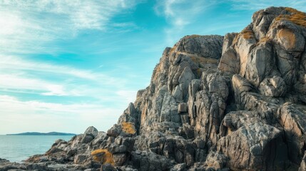Majestic rocky cliffs extend towards the serene blue sea, under a clear sky with light clouds. Perfect natural landscape scenery.