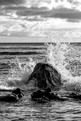 Black lava rocks in the surf at the &ldquo;Pointe aux Piments&rdquo; in the west of the tropical vacation paradise of Mauritius (Indian Ocean). Breaking wave with water droplets, splashes, foam and spray. 