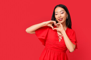 Beautiful Asian woman making heart with her hands on red background