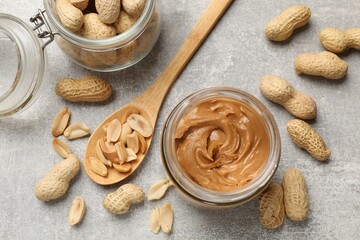 Tasty peanut butter in jar and groundnuts on grey textured table, flat lay