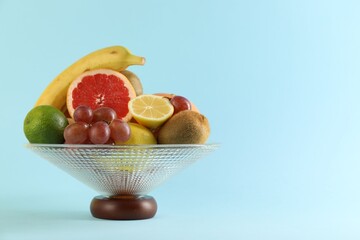 Glass vase with different fresh fruits on light blue background. Space for text
