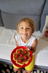 Sweet toddler birthday boy, eating belgian waffle with strawberries and chocolate
