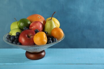 Glass vase with different fresh fruits on light blue wooden table, space for text