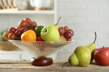 Glass vase with different fresh fruits on wooden table, closeup