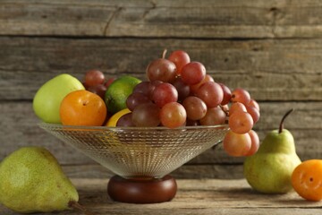 Glass vase with different fresh fruits on wooden table, closeup