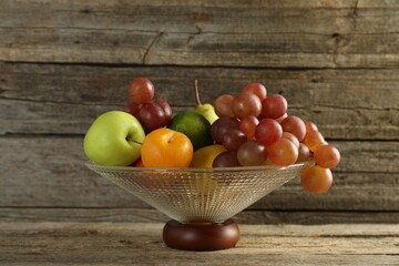 Glass vase with different fresh fruits on wooden table