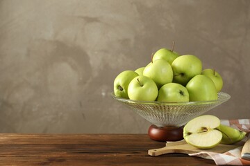 Glass vase with fresh green apples on wooden table against gray background, space for text