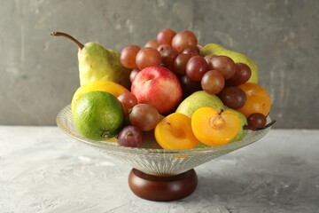 Glass vase with different fresh fruits on gray textured table, closeup
