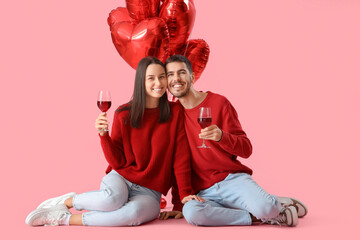 Happy young couple with glasses of wine and balloons on pink background. Valentine's Day celebration