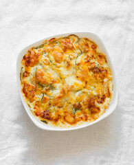 Casserole with potatoes, zucchini, salmon, spinach and cheese in a baking dish on a light surface