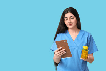Obraz premium Beautiful young female doctor with clipboard and pills on blue background
