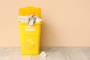 Full trash bin with PAPER sign near beige wall. Recycling concept