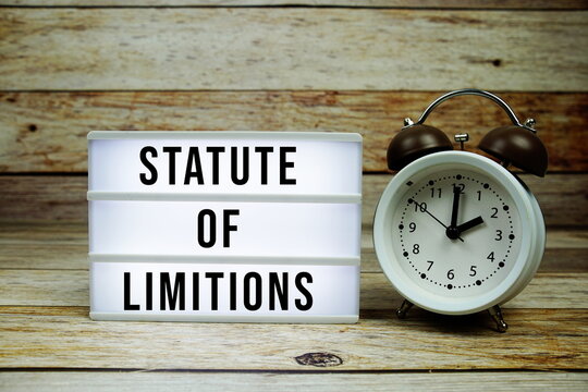 Statute of Limitions text on LED lightbox with alarm clock on wooden background