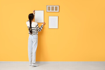 Young woman hanging picture frame on orange wall in room