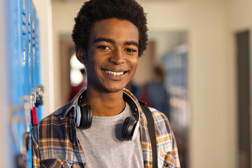 Smiling teenager with headphones standing by lockers in high school hallway © wavebreak3