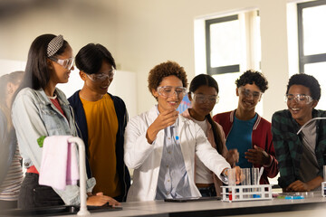 Wearing safety goggles, students in high school observing teacher conducting science experiment
