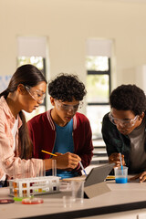 Conducting science experiment, teenagers using tablet and lab equipment in high school