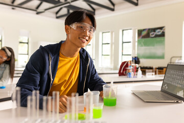Conducting science experiment with laptop and test tubes, teenager in high school classroom © WavebreakMediaMicro