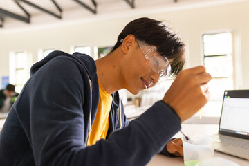 In high school, teenager conducting science experiment with laptop and safety goggles