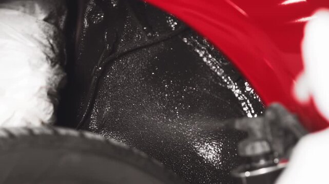 Close-up footage of a black undercoating or rust prevention liquid being sprayed onto a car's undercarriage