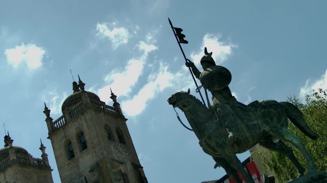 A statue with a man on a hourse in front of a church tower in Porto.
