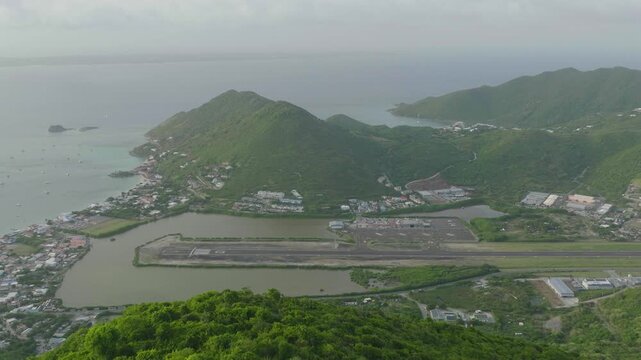Aeria moving shot of Grand Case Airport with plane departing in Saint Martin with beautiful Caribbean landscape at background.