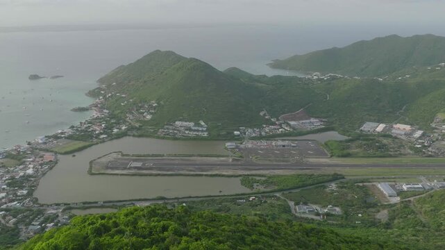 Pull back shot of Grand Case Airport with green mountain in foreground in Saint Martin. Drone view.