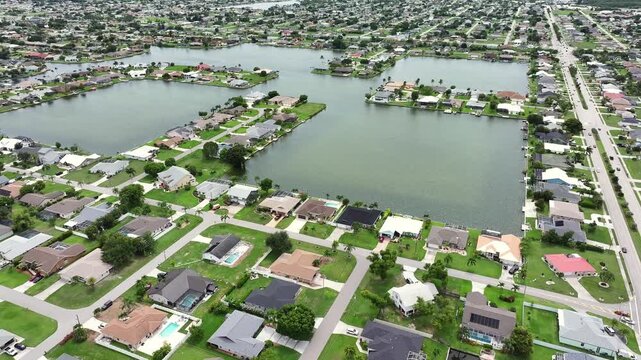 Suburban neighborhood with waterfront properties and green lawns. Located in Florida, showcasing residential houses and intersecting canals. Aerial orbit.