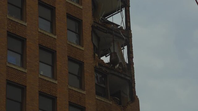 A close-up of the demolition process of an ornate high-rise building in Youngstown, Ohio. The top floors with decorative elements are being dismantled by a crane with a wrecking ball.