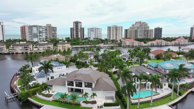 Luxury waterfront homes in Naples, Florida with pools and private docks. High-rise buildings in the background. Aerial.