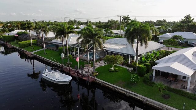 Waterfront homes with boat docks and palm trees in Florida. American flag and lush gardens by the canal. Aerial.