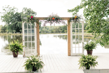Wedding arch with flowers and greenery on a lakeside platform.