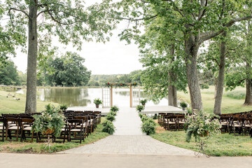 Outdoor wedding ceremony by a lake with decorated chairs and arch.