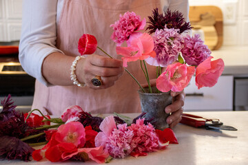 Woman arranging a bouquet of poppies in a vase on a kitchen counter