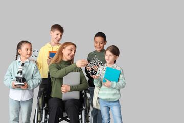 Mature science teacher in wheelchair with laptop and little pupils on light background