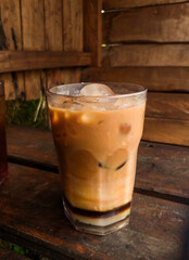 a glass of coffee with palm sugar served on a wooden table
